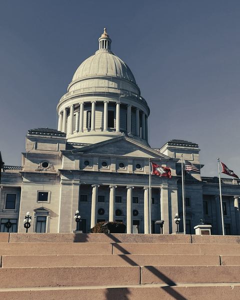 A state capitol building with flags in front of its steps