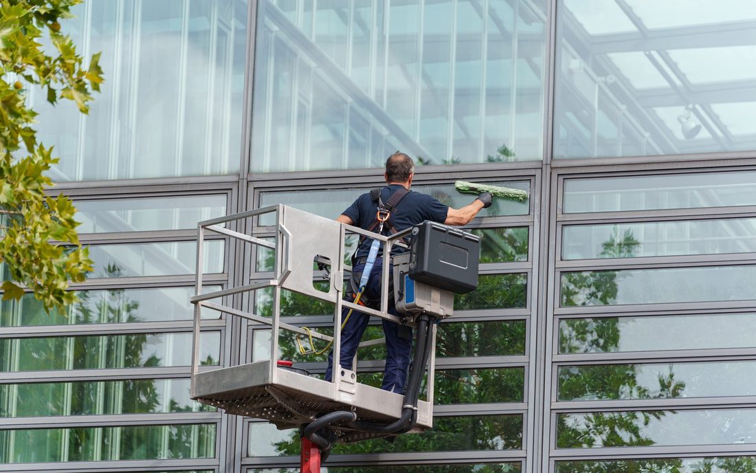 A technician cleaning the glass facade of an office building from a lift platform