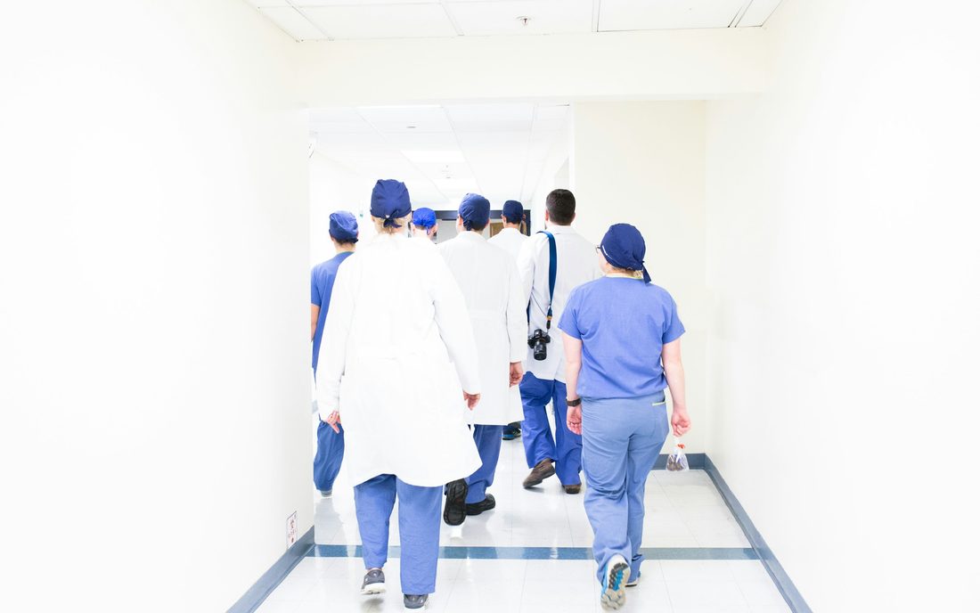 Clinical staff in scrubs and white coats walking down a hospital corridor